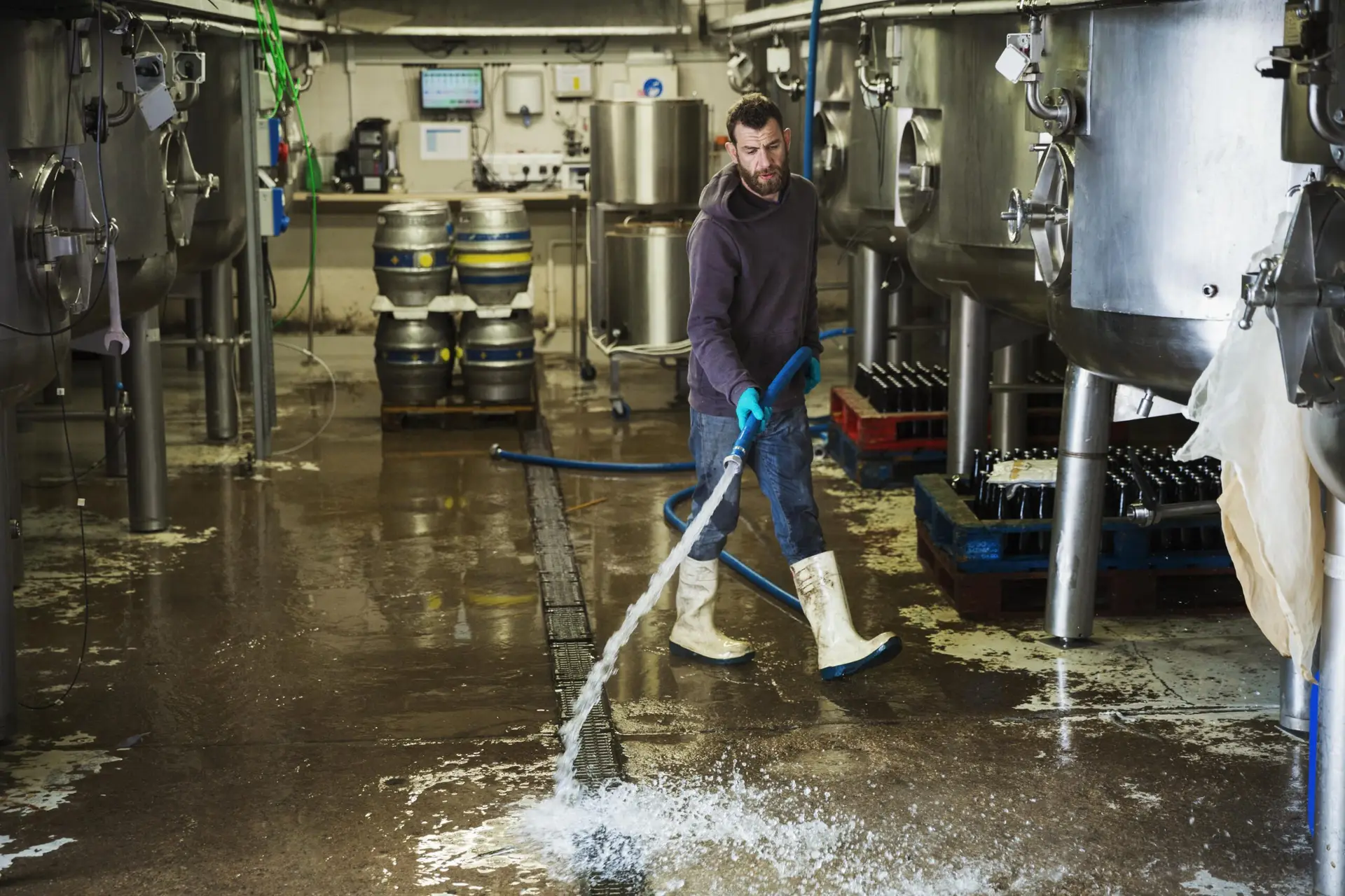 Reinigungskraft arbeitet in einer Brauerei und reinigt den Boden mit Wasserschlauch.
